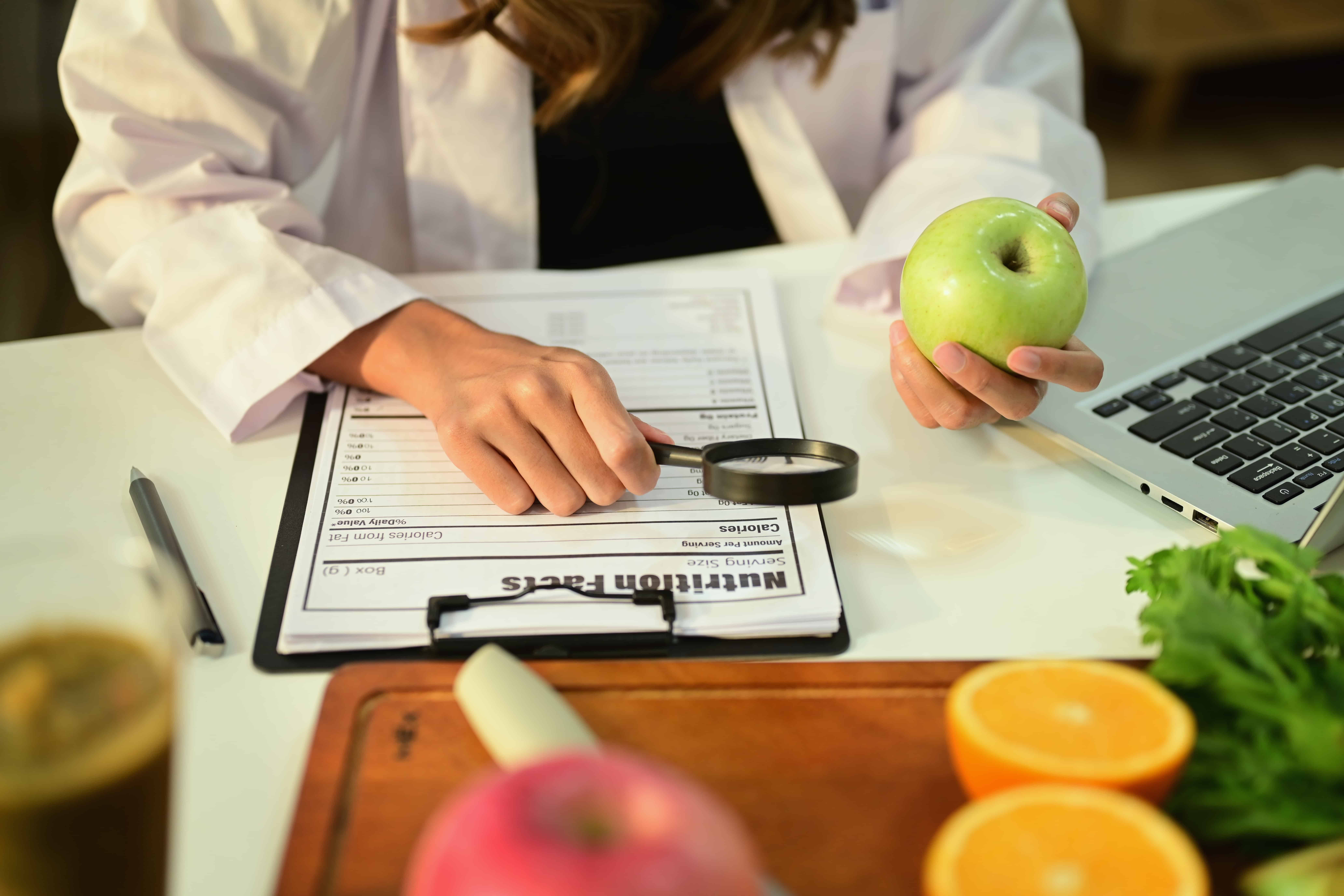 Nutritionist Holding Fruit and Prescribing Recipe at Desk