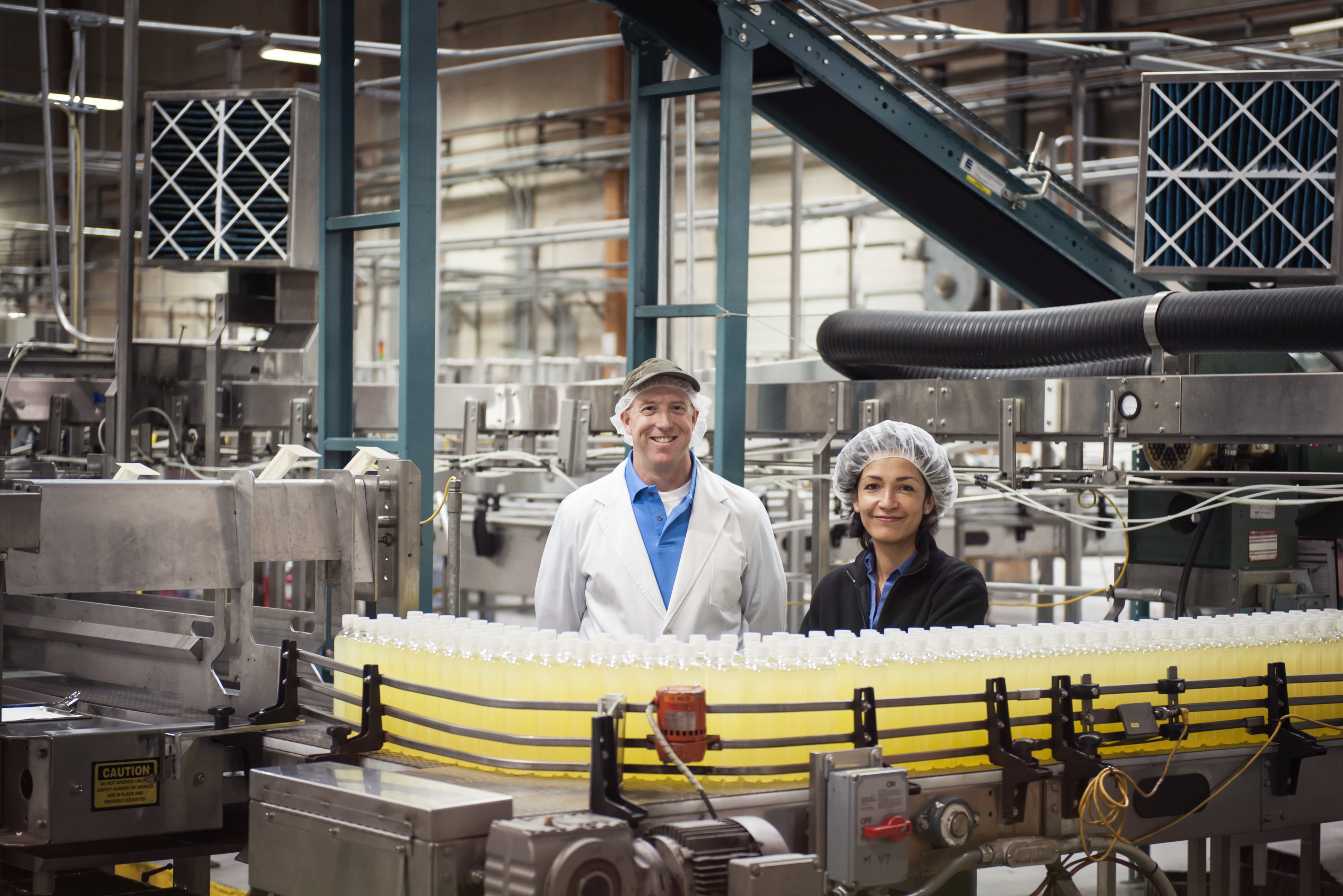 Two Workers by a Conveyor Belt in a Bottling Plant